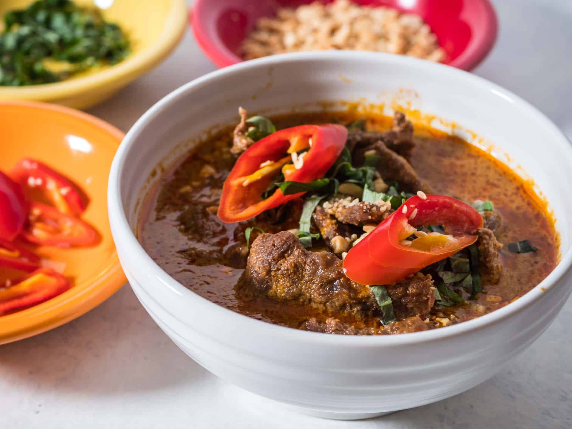 A bowl of panang curry topped with sliced basil and hot peppers