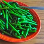 A platter of cooked green beans with a serving spoon