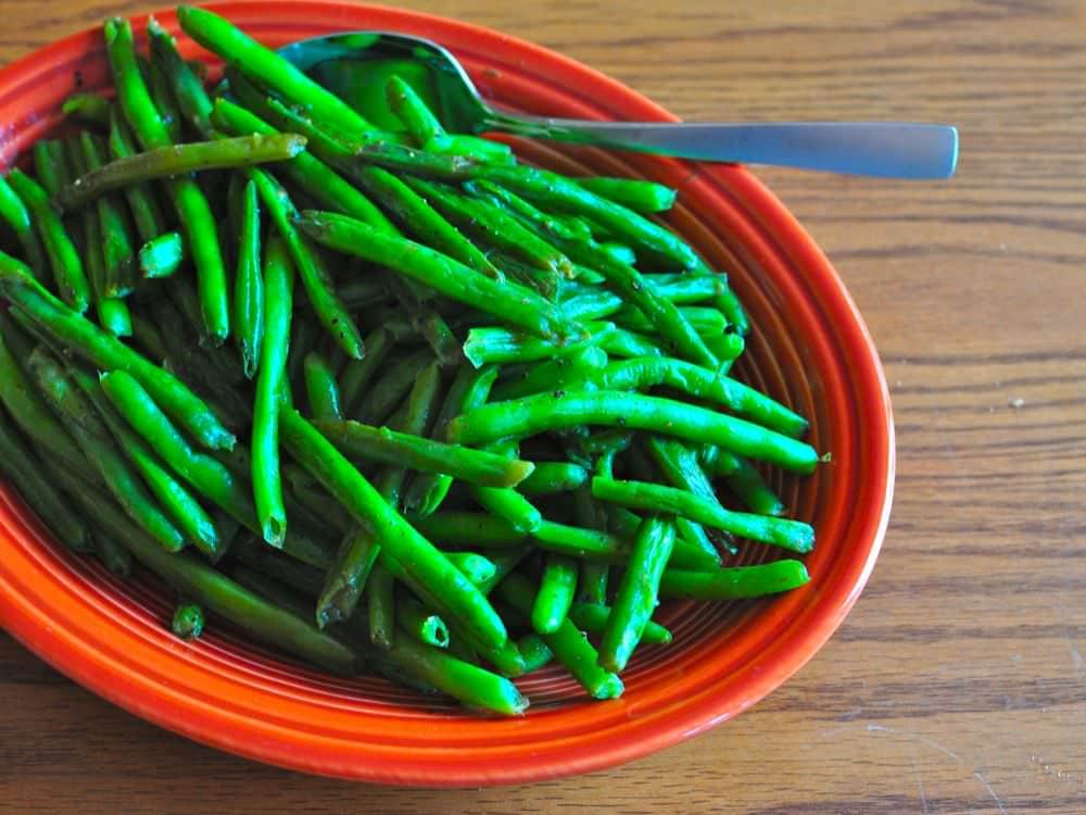 A platter of cooked green beans with a serving spoon