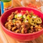 A bowl of chili mac topped with green onions and pickled jalapenos