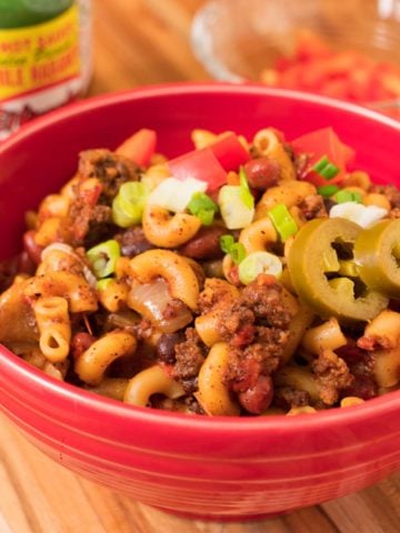 A bowl of chili mac topped with green onions and pickled jalapenos