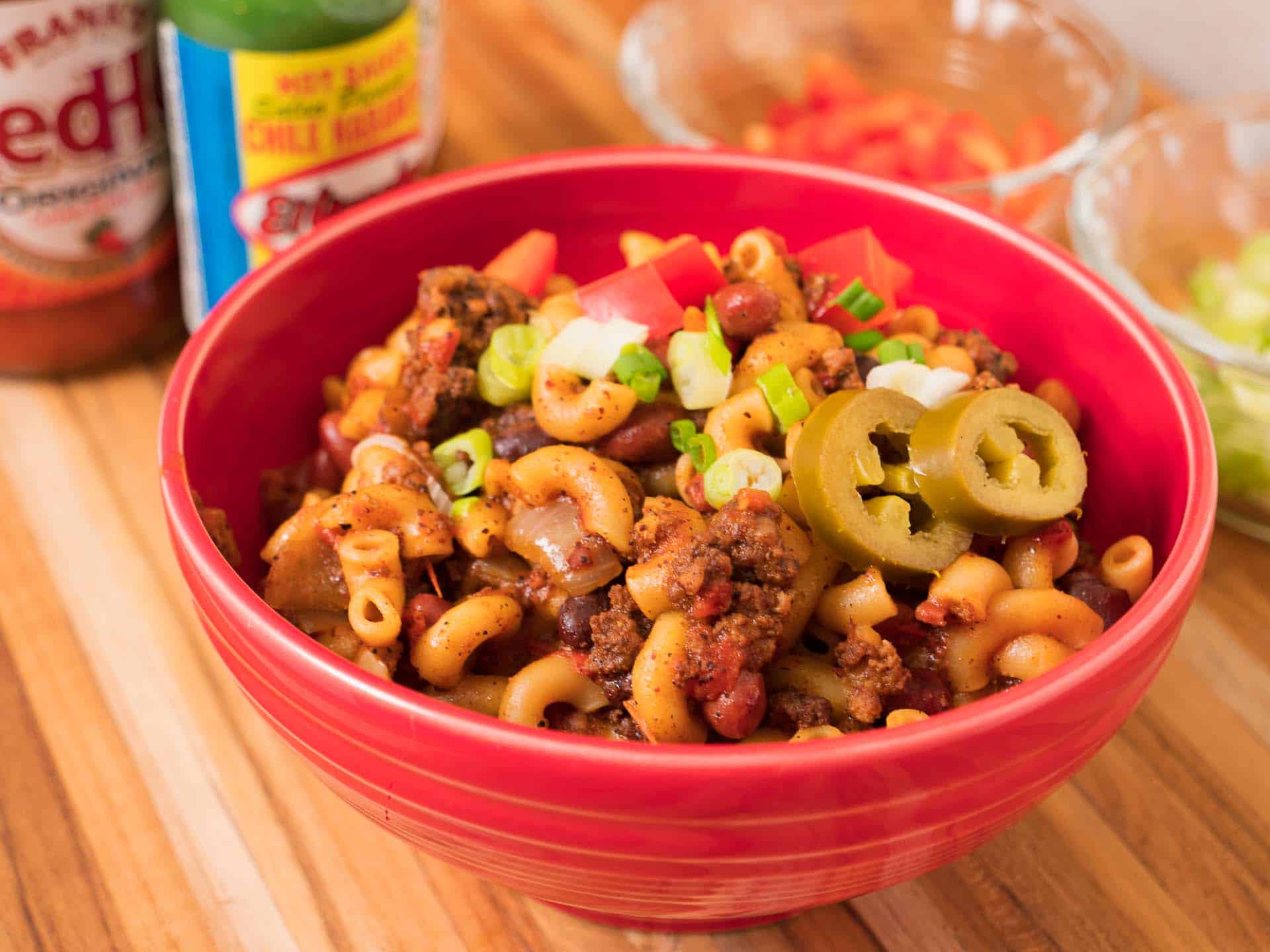 A bowl of chili mac topped with green onions and pickled jalapenos