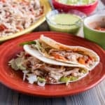 Quick Chicken Tacos on a plate with a platter of chicken and other toppings in the background