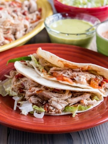 Quick Chicken Tacos on a plate with a platter of chicken and other toppings in the background