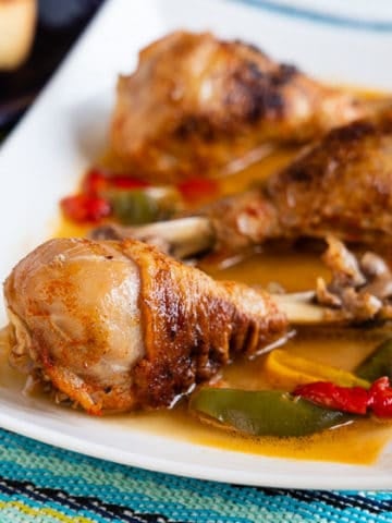 Chicken drumsticks with peppers and paprika on a white platter
