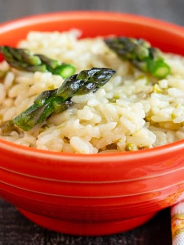 An orange bowl full of asparagus risotto with a napkin
