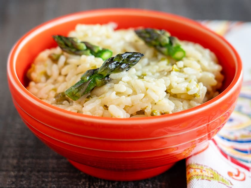 An orange bowl full of asparagus risotto with a napkin