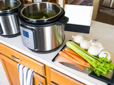 A kitchen island with two instant pots, a pile of vegetables on a cutting boad, a chef's knife, and an iPad in the background