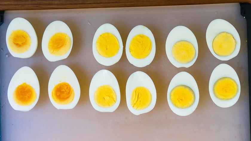 Hard-boiled egg halves on a cutting board, 4 undercooked, 4 cooked just right, 4 overcooked