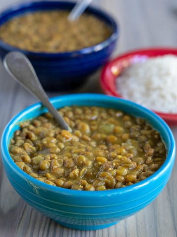 A blue bowl of lentils with a spoon in the foreground, with a bowl of rice and another bowl of lentils in the background