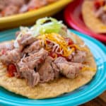 Pork taco topped with salsa, shredded cheese, and shredded lettuce on a teal plate