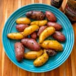 An overhead picture of a blue bowl full of multicolored fingerling potatoes, coated with herbs, with a jar of Herbes de Provence and a bottle of olive oil on the side