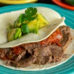 Flank steak tacos on an aqua plate, topped with avocado and cilantro