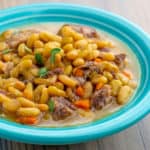 A teal bowl of cooked flageolet beans with chunks of lamb and carrot and a sprinkling of thyme leaves on top from the recipe Instant Pot Flageolet Beans with Lamb