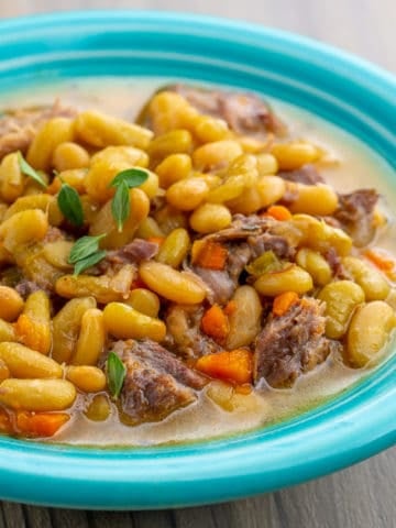 A teal bowl of cooked flageolet beans with chunks of lamb and carrot and a sprinkling of thyme leaves on top from the recipe Instant Pot Flageolet Beans with Lamb