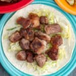 A pile of pork carnitas on shredded lettuce, piled on a tortilla, on an aqua plate