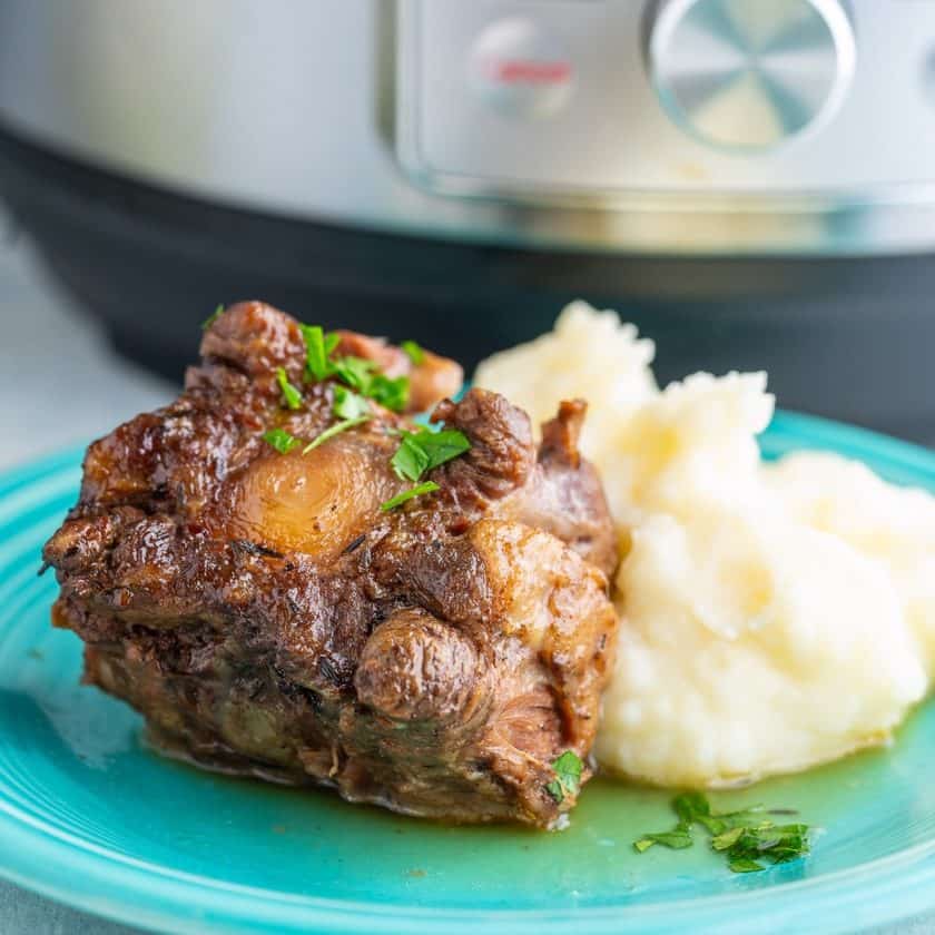 Cooked oxtail sprinkled with parsley propped up against mashed potatoes on a teal plate with the text Instant Pot Easy Braised Oxtail underneath