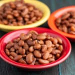 Three bowls of cooked Pinto Beans on a wood tabletop