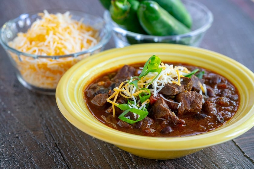 A bowl of steak chili sprinkled with shredded cheese and green onions