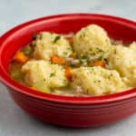 A red bowl of Turkey Soup with Mashed Potato Dumplings on a white background