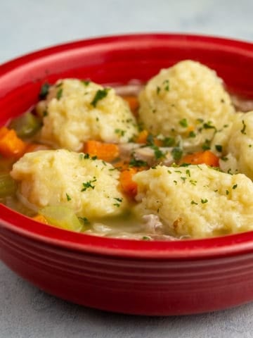 A red bowl of Turkey Soup with Mashed Potato Dumplings on a white background