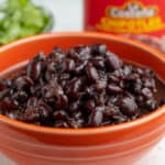 Cooked black beans in an orange bowl with a jar of chipotles behind it