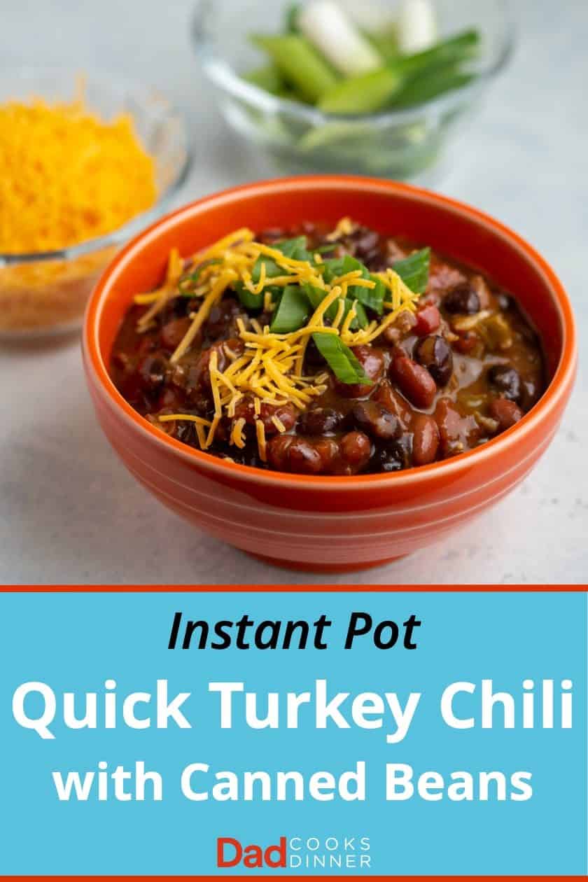 An orange bowl of turkey and bean chili, sprinkled with cheese and green onions, with a bowl of cheese and green onions in the background