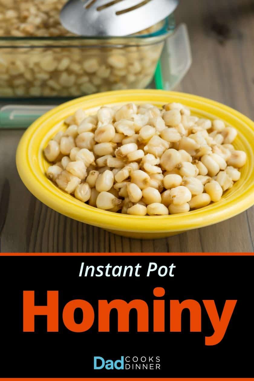 A yellow bowl of cooked hominy on a wooden tabletop, in front of a storage container of hominy