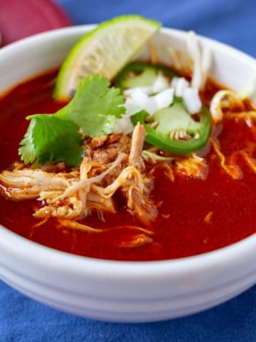 Bowl of Mexican Chicken Soup in Red Chile broth, with shreds of chicken, cilantro leaves, jalapeno slices, and diced onion on top