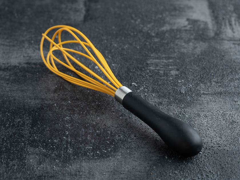Yellow silicone whisk with a black handle on a black background