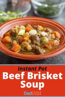 A bowl of beef brisket soup with carrots, green onions, and thyme, in an orange bowl on a slate-gray background