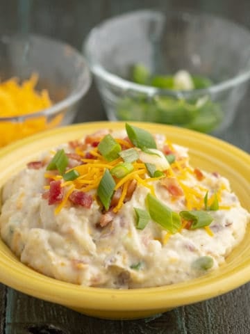 A bowl of loaded smashed red potatoes with bacon, shredded cheddar, and sliced green onions
