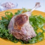 Cooked duck leg on a bed of lettuce, on a yellow plate