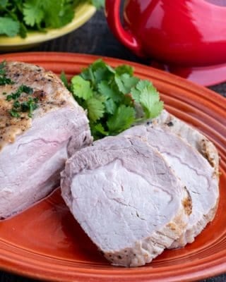 A sliced pork loin roast on an orange platter, with parsley and a gravy boat in the background