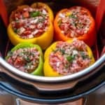 Four uncooked stuffed peppers in red, yellow and green, inside Instant Pot