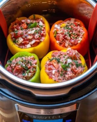 Four uncooked stuffed peppers in red, yellow and green, inside Instant Pot