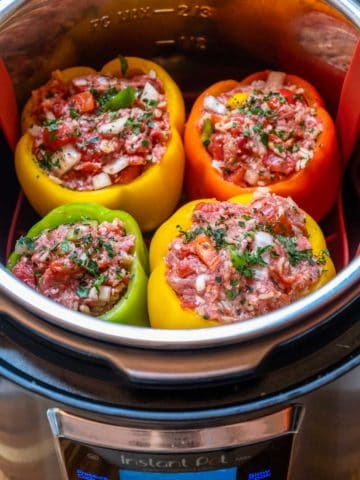 Four uncooked stuffed peppers in red, yellow and green, inside Instant Pot