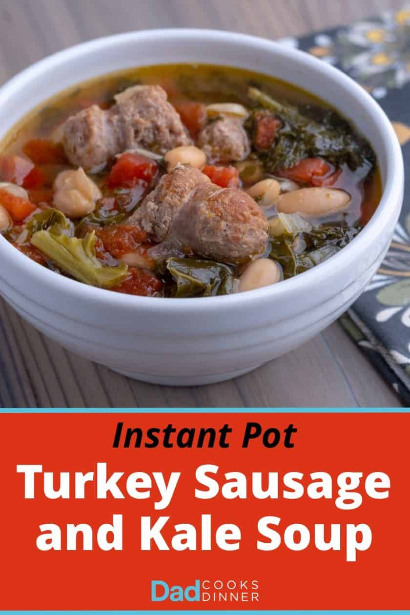 A white bowl of turkey sausage and kale soup, with beans and tomatoes, on a wooden table with a napkin.