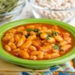 A bowl of cooked cannellini beans with tomatoes and pancetta, sprinkled with parsley, on a colorful napkin