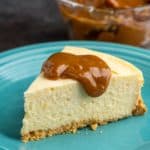 A piece of cheesecake with a dollop of dulce de leche on an aqua plate with a bowl of dulce de leche in the background