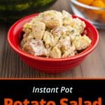 A red bowl of potato salad, on a wooden table, in front of a bowl of cherry tomatoes and a watermelon.