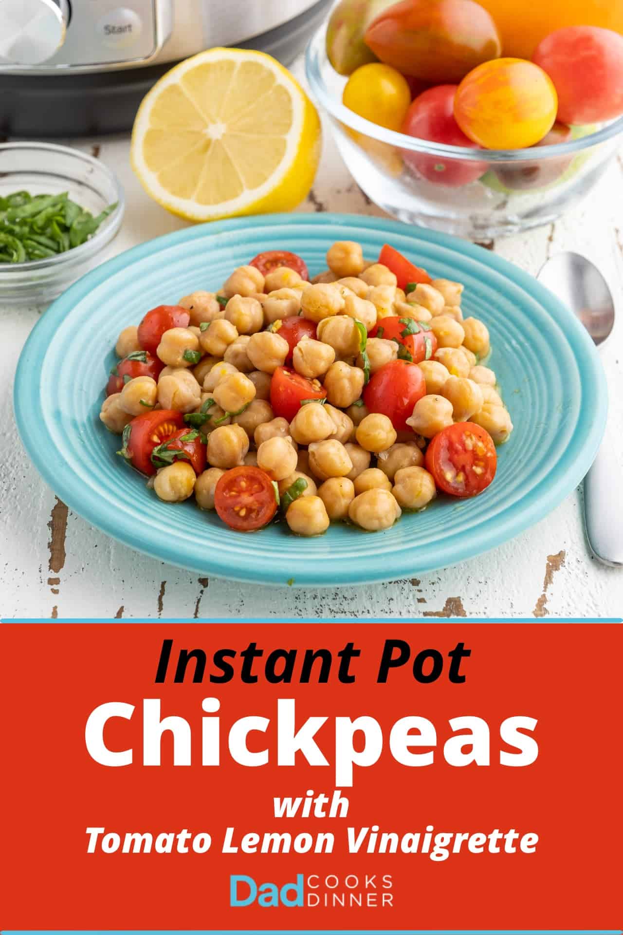 A plate of chickpeas with tomato lemon vinaigrette on a white table, with an Instant Pot, some minced basil, a half a lemon, and a bowl of tomatoes in the background.