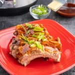 A sliced rack of baby back ribs sprinkled with green onions with an Instant Pot and bowl of glaze in the background