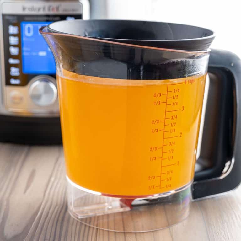 A fat separator full of rotisserie chicken broth, with an instant pot in the background