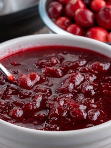 A bowl of cranberry sauce with a bowl of cranberries and an Instant Pot in the background
