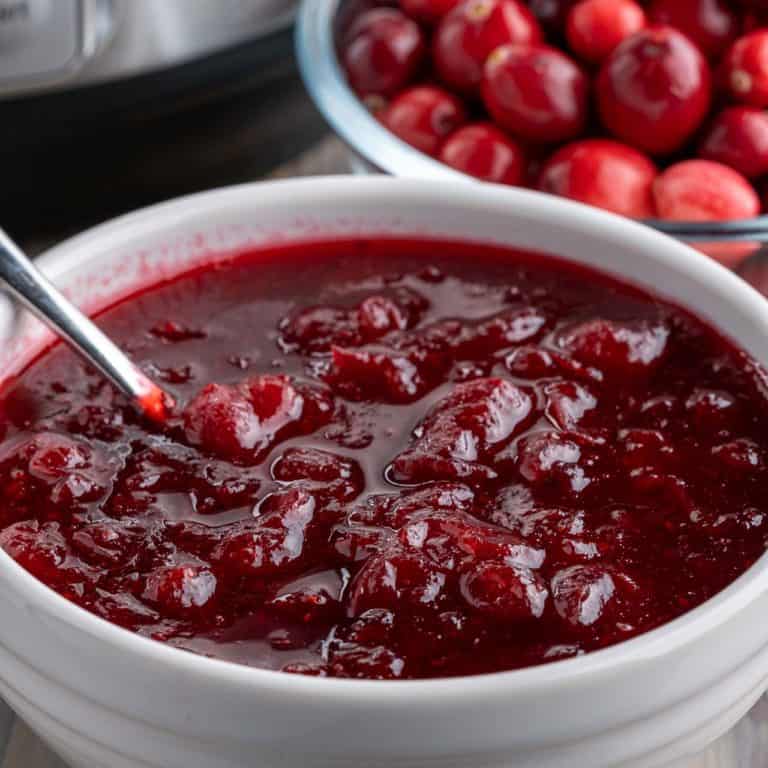 A bowl of cranberry sauce with a bowl of cranberries and an Instant Pot in the background