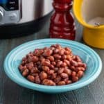 A bowl of red beans in front of a pressure cooker, a salt pig, and a pepper grinder