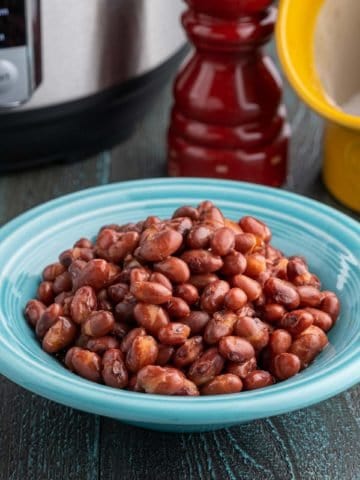 A bowl of red beans in front of a pressure cooker, a salt pig, and a pepper grinder