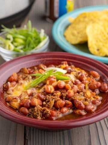 A bowl of turkey and small red bean chili, with minced green onions, tortilla chips, and an Instant Pot in the background.