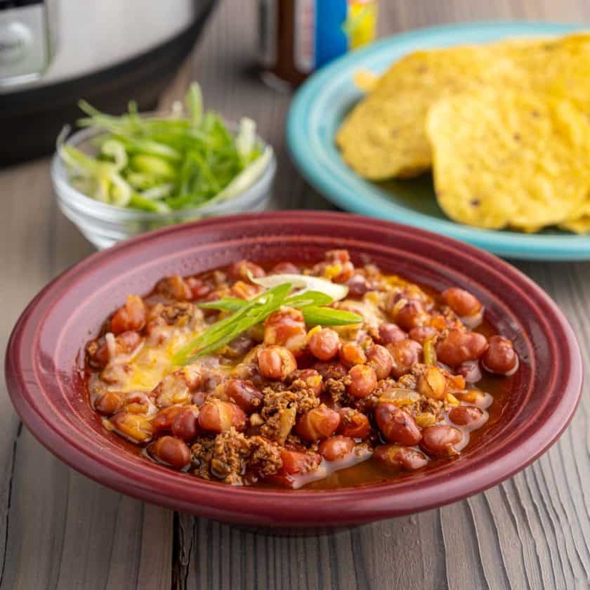A bowl of turkey and small red bean chili, with minced green onions, tortilla chips, and an Instant Pot in the background.